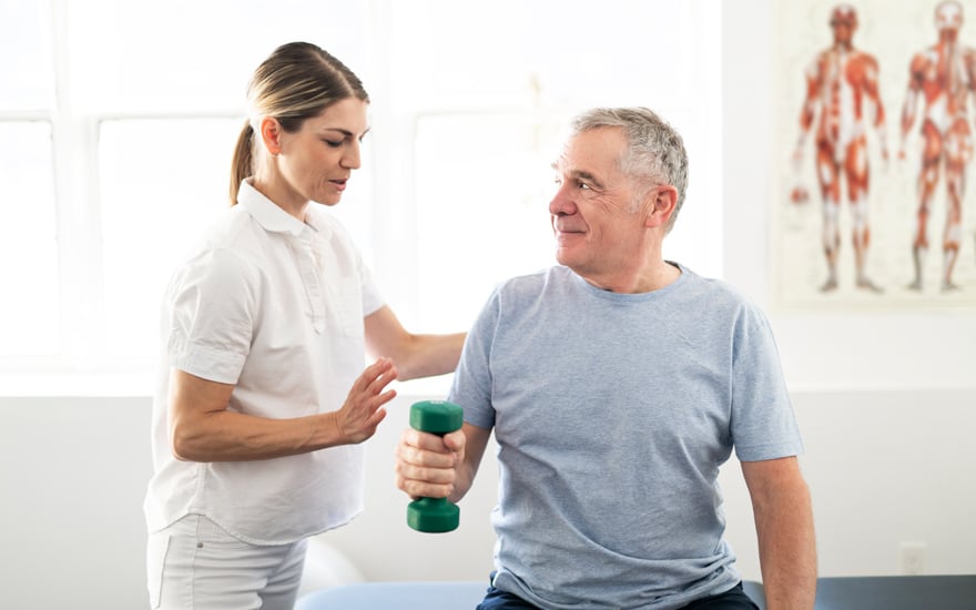 A physical therapist guides an older adult male through shoulder strengthening exercises