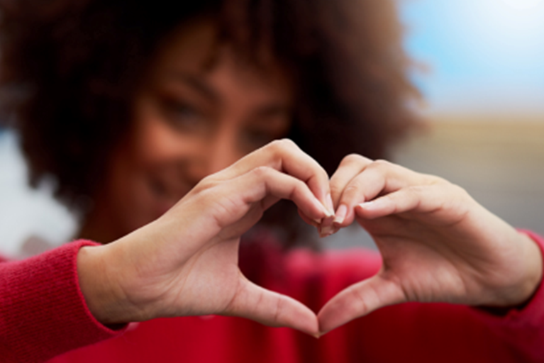 A Black female olds her hands in the shape of a heart.