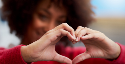 A Black female olds her hands in the shape of a heart.
