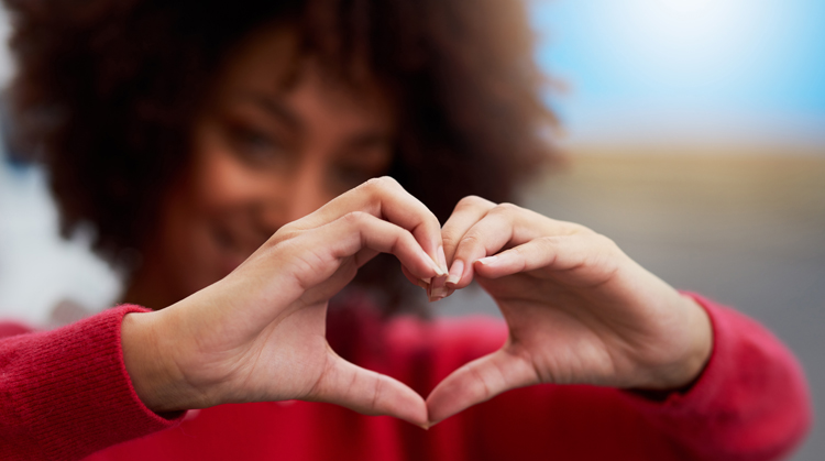 A Black female olds her hands in the shape of a heart.