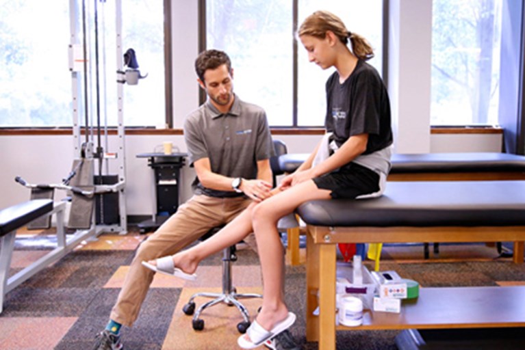 A teen with a physical therapist for treatment of knee pain.