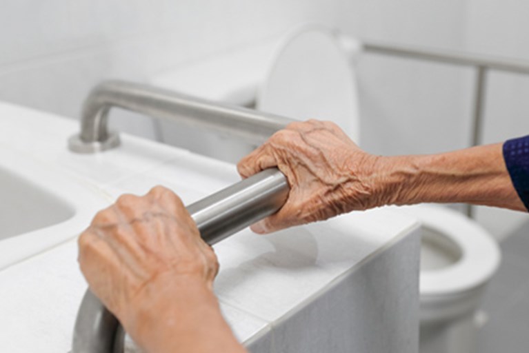 Older adult hands holding a bathroom safety rail.