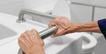 Older adult hands holding a bathroom safety rail.