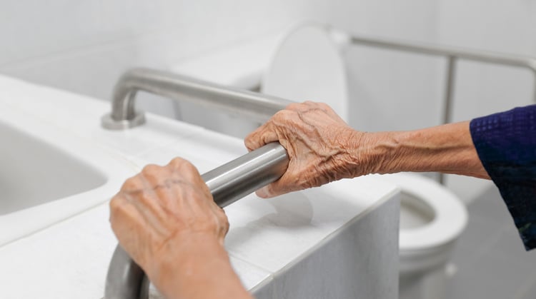 Older adult hands holding a bathroom safety rail.