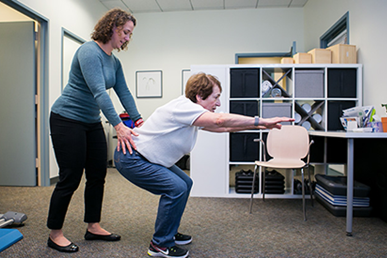 Patient squatting while physical therapist provides instruction.