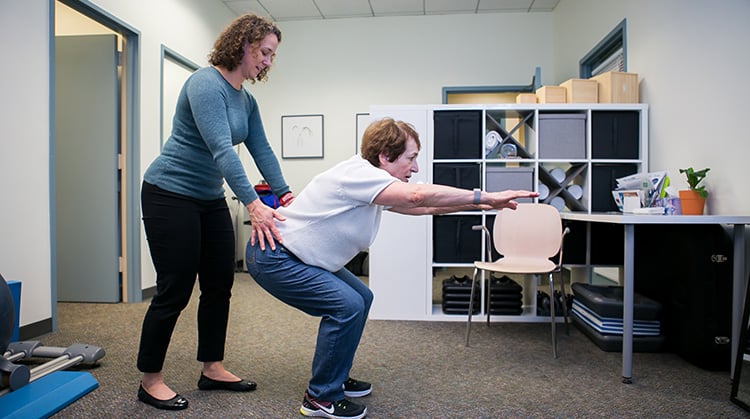 Patient squatting while physical therapist provides instruction.