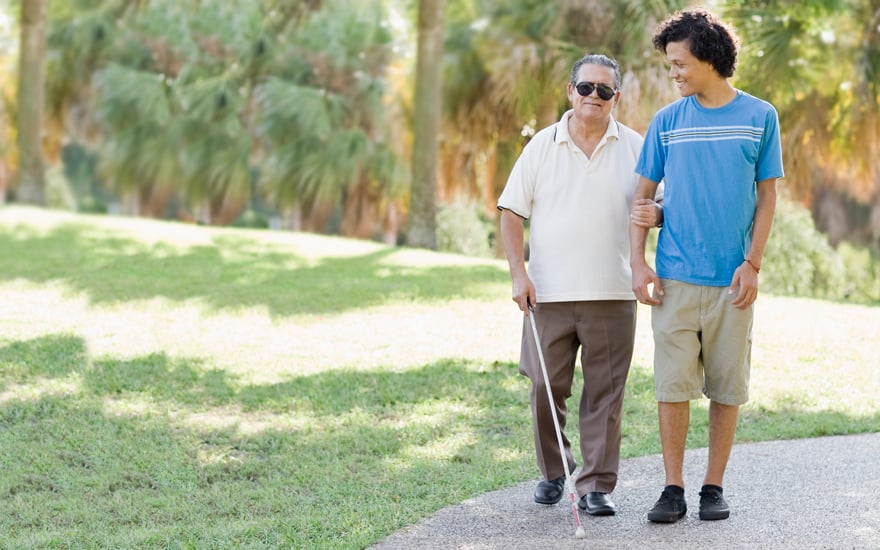 A man who is blind walking outdoors with his grandson.