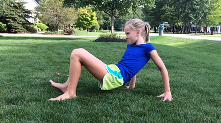 A young person doing the crab walk activity on the grass 