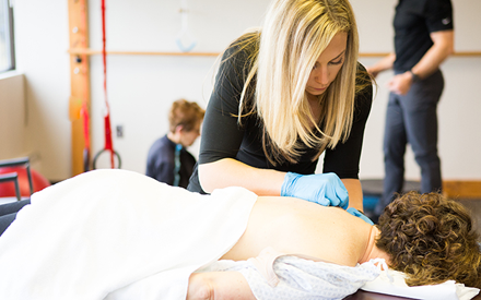 A PT performing dry needling on a person's shoulder.