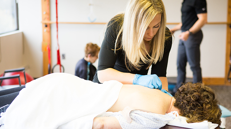 A PT performing dry needling on a person's shoulder.