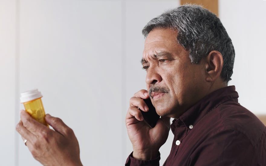 A hispanic man holding a prescription drug bottle while talking on the phone.