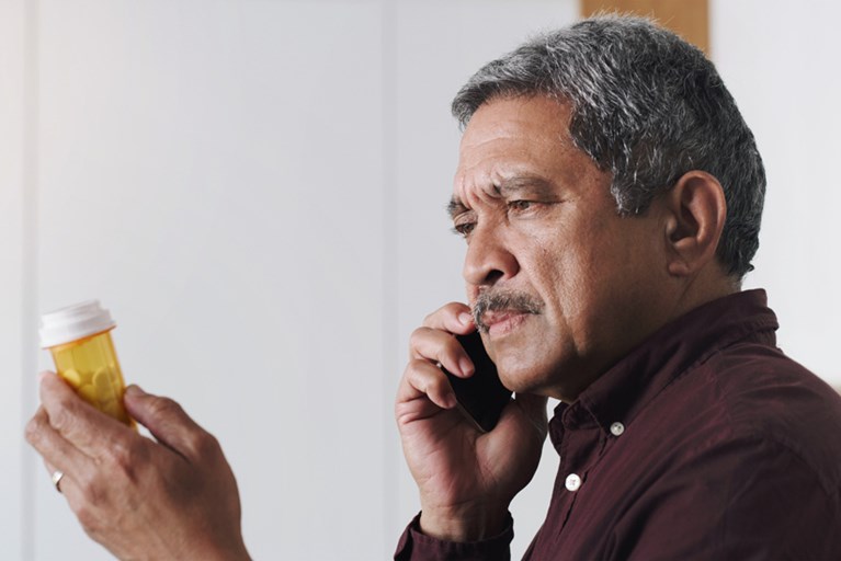 A hispanic man holding a prescription drug bottle while talking on the phone.