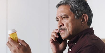 A hispanic man holding a prescription drug bottle while talking on the phone.