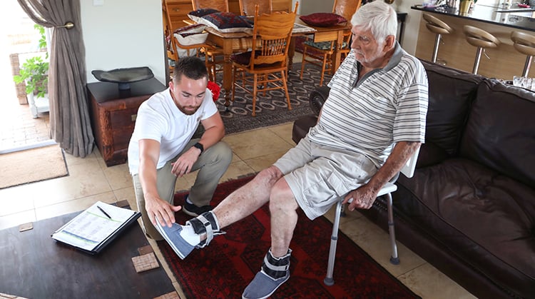 Physical Therapist kneeling down to assist patient sitting in chair with leg excercise.