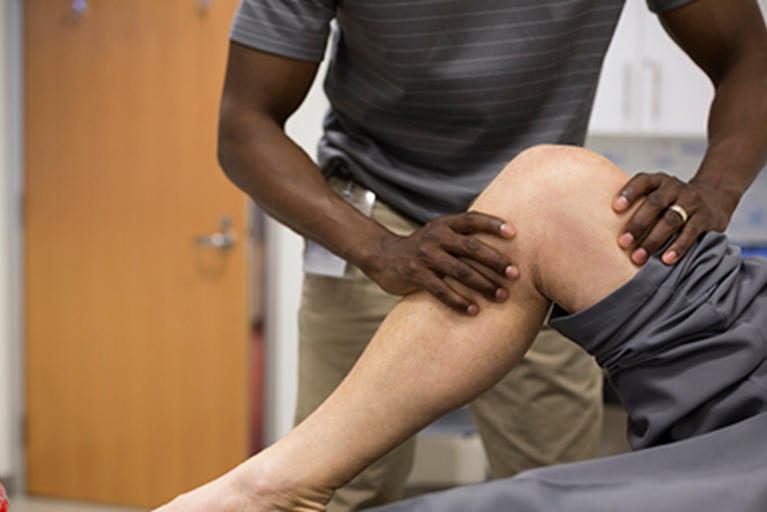 A physical therapist uses hands on therapy on a person's knee.