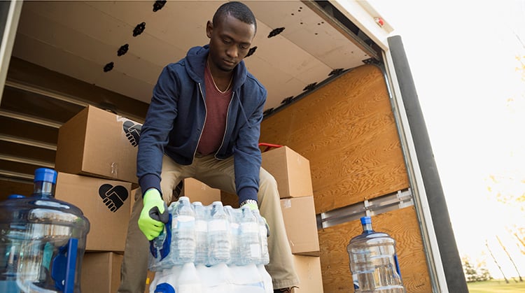 Man lifting water bottles out of moving van.