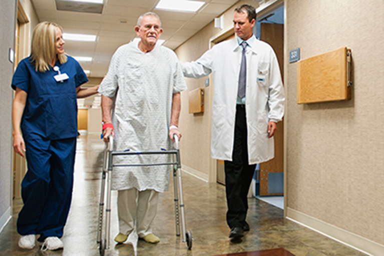 Male patient walking with a physical therapist and doctor in a hospital