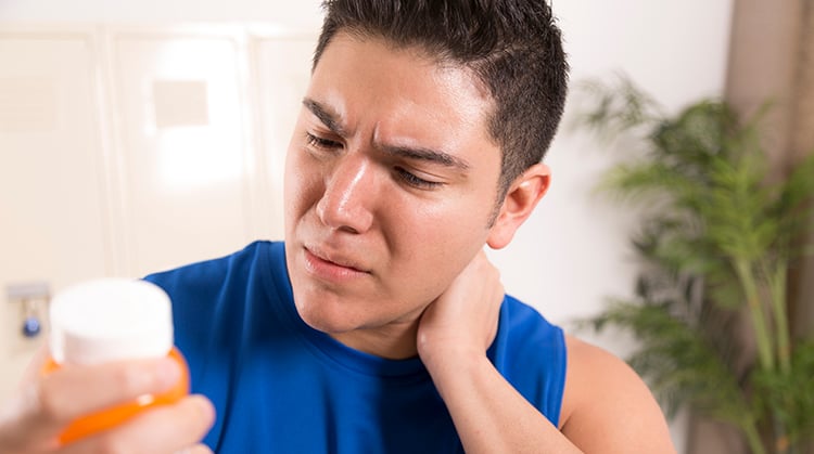 A man looking at a prescription bottle while holding his neck in pain.