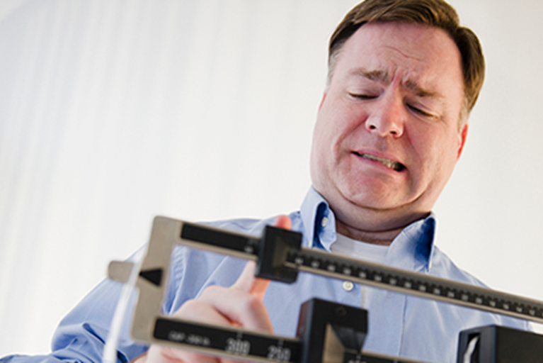 Man standing on scale grimacing.