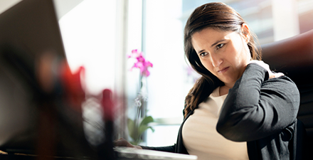 Woman holding neck in office setting.