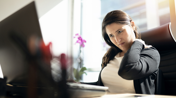 Woman sitting at office desk rubbing her neck.