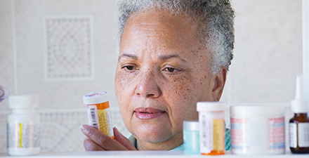 Woman taking medicine bottle out of medicine cabinet.