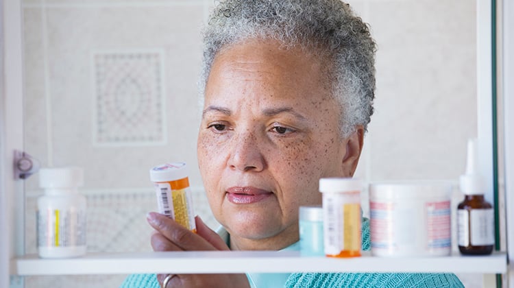 Woman taking medicine bottle out of medicine cabinet.