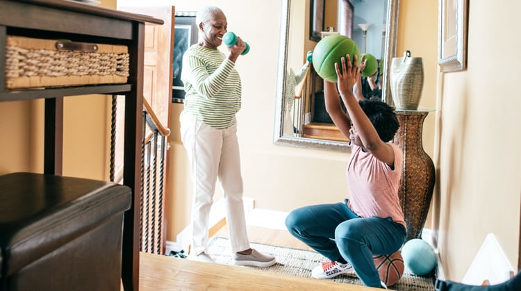 An older adult lifts weights while young family member exercises with a ball.