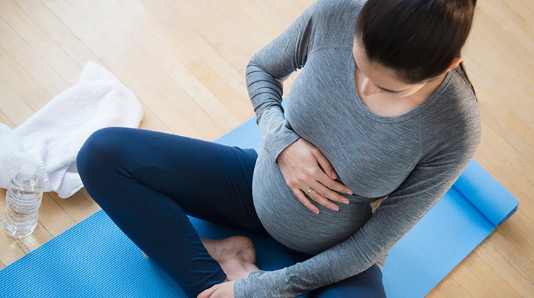 Pregnant woman sitting on yoga mat.