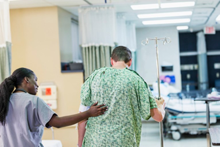A PT helping  a patient walk very soon after surgery.