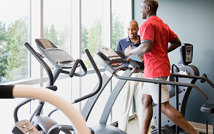 A man running on a treadmill as his physical therapist looks on.