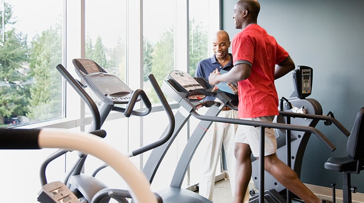 A man running on a treadmill as his physical therapist looks on.