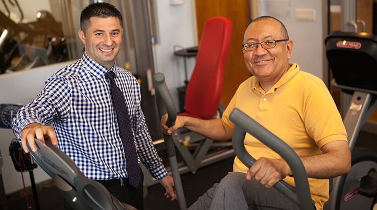 Physical Therapist standing next to a patient on a recumbent bike.