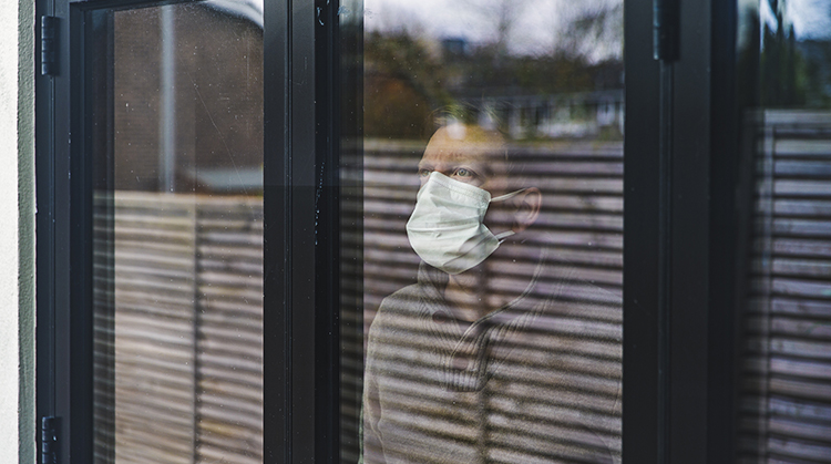 Masked man starring outside behind window.