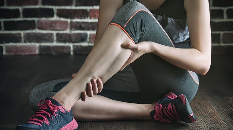 A woman holding her lower leg in pain.