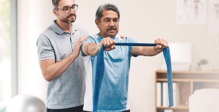 A physical therapist leads a man through strengthening exercises using an elastic band.