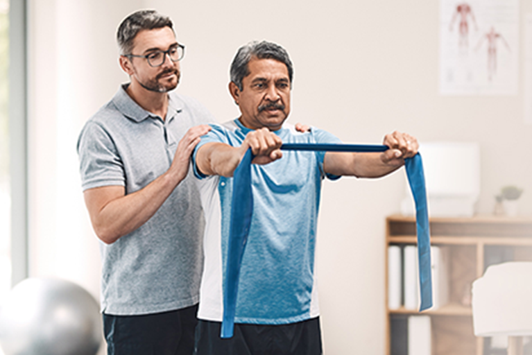 A physical therapist leads a man through strengthening exercises using an elastic band.