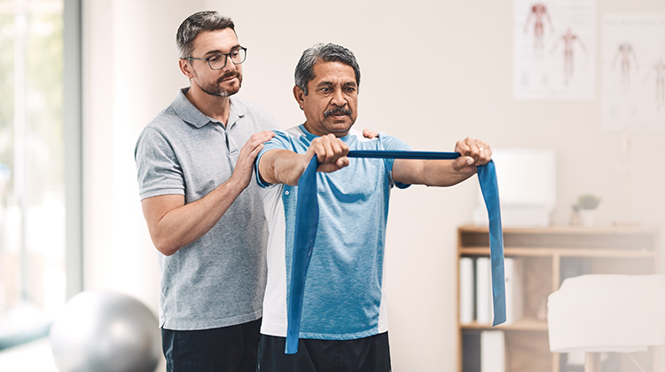 A physical therA physical therapist leads a man through strengthening exercises using an elastic band.apist helps a person doing strengthening exercises with an elastic band.