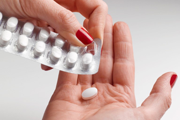 A woman pushes a pill out of a blister pack.