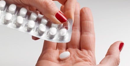 A woman pushes a pill out of a blister pack.