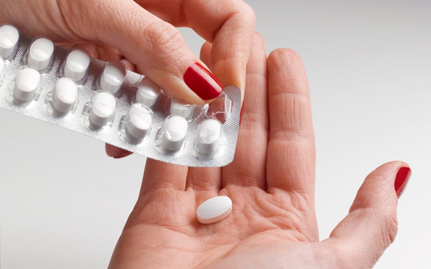 A woman pushes a pill out of a blister pack.