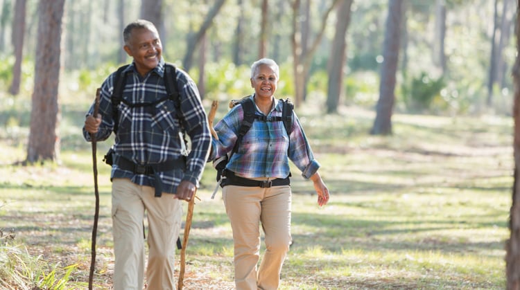 An older couple walking outside in the woods for exercise.