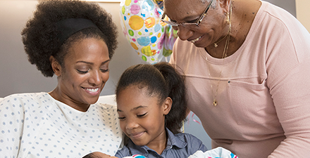 Three generations of women looking at a newborn.