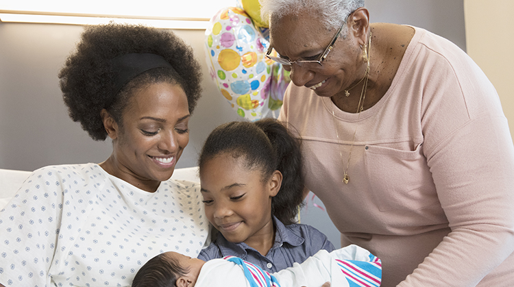 Three generations of women looking at a newborn.