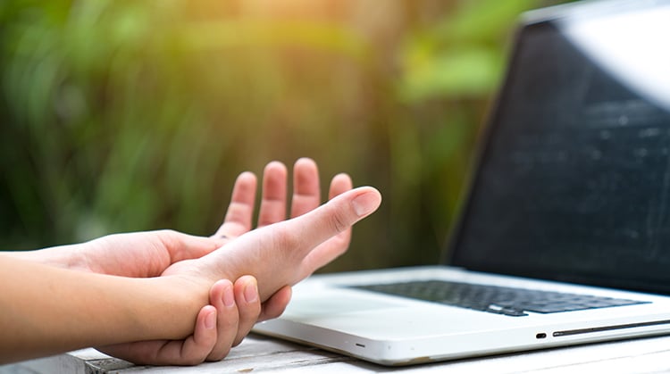 Person holding their wrist in pain in front of computer